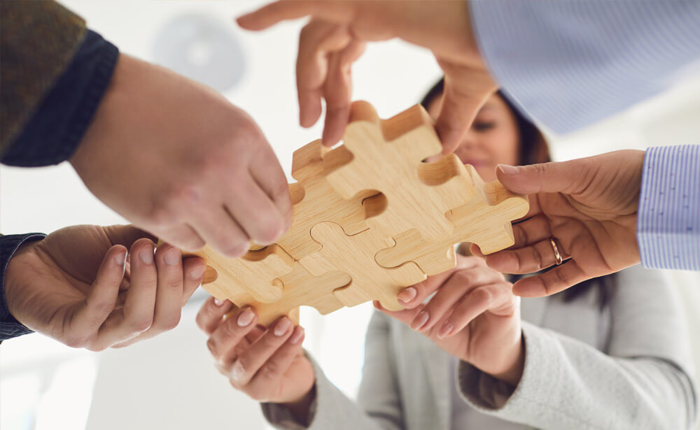 A diverse business team collaboratively assembling puzzle pieces on a table. This image illustrates the concept of trust-building through teamwork, cooperation, and problem-solving. Each team member contributes their unique skills and perspectives, symbolizing the importance of mutual reliance and cohesion in fostering trust within the business environment.